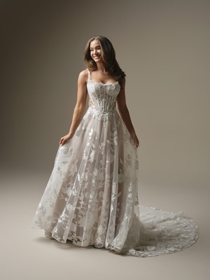 Natalie Marie by Maggie Sottero A-line wedding dress with floral lace overlay, sheer bodice, delicate straps, and flowing illusion train