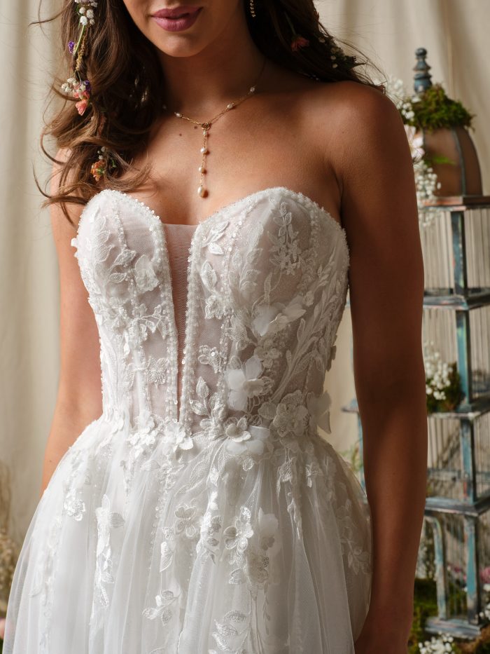 Nora by Rebecca Ingram strapless wedding dress featuring illusion plunge neckline, sheer bodice, and detailed 3-D floral lace applique